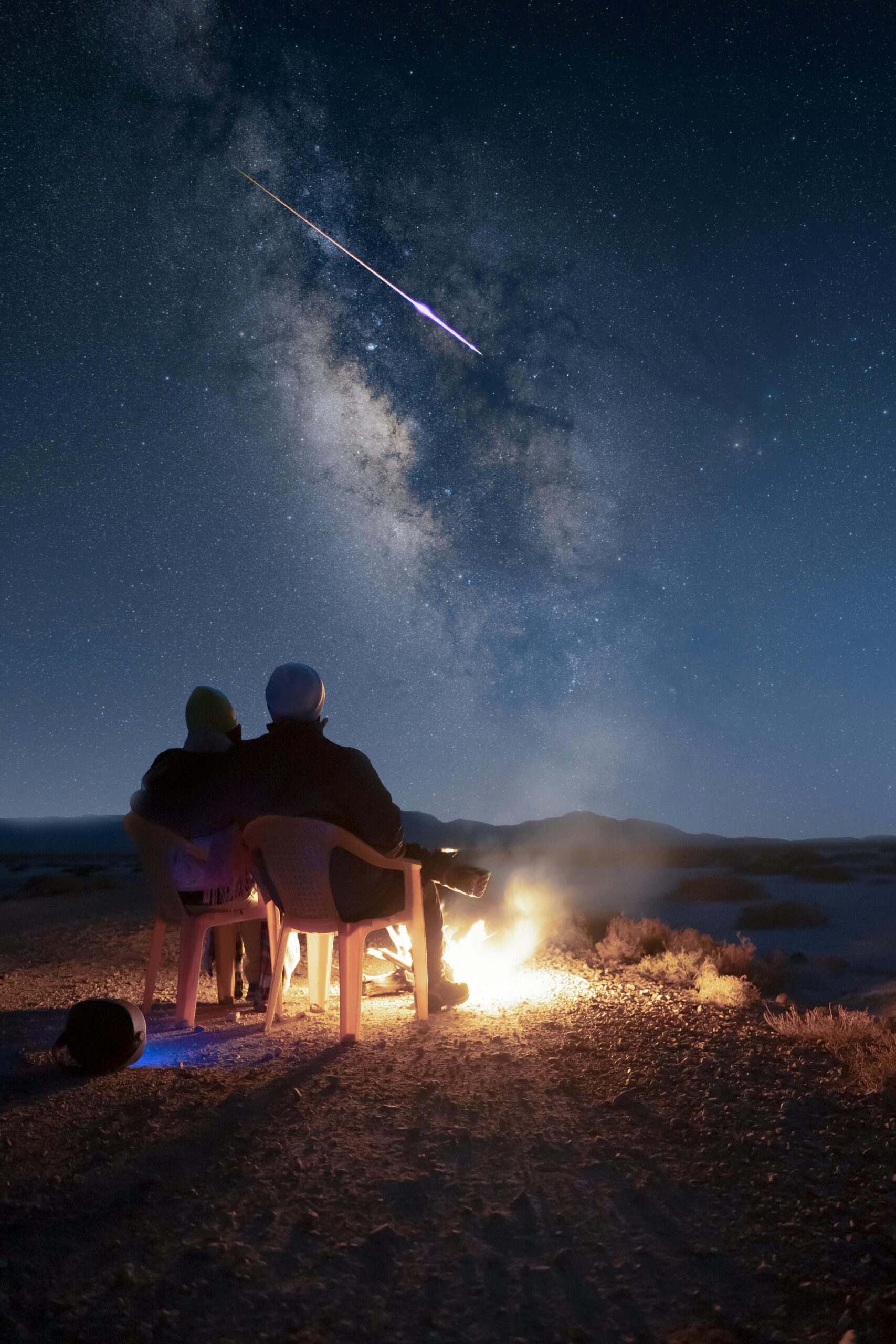 Couple enjoying a campfire under the Milky Way in Iran with a shooting star in view.